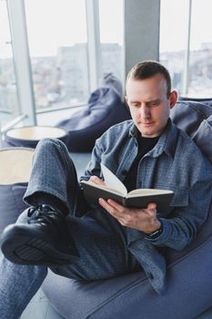A male businessman in a casual suit resting in a comfortable pouf while working, an attractive freelancer in a suit works remotely and checks notes in a notebook