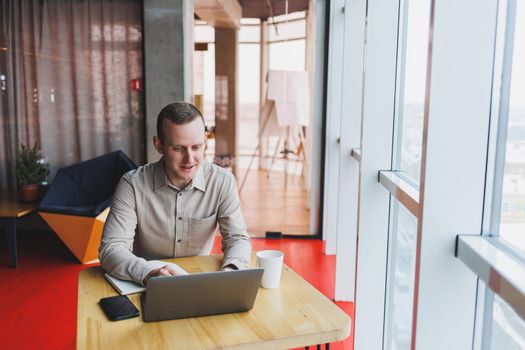 Smart young man looking for information on a website and working as a freelancer on developing a graphic project on a modern laptop using a wireless internet connection in a cafe interior