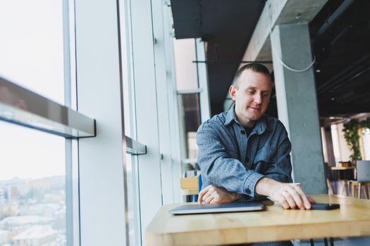 Handsome male manager sits at a table in a modern office with a closed laptop and rests, remote work
