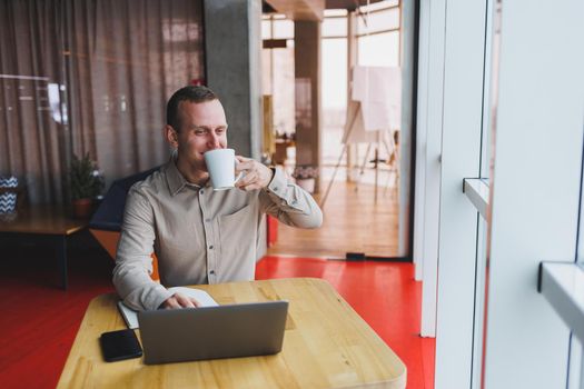 Intelligent young male using laptop to take notes during online education program, experienced male freelancer sitting with technology in cafe interior. Young businessman