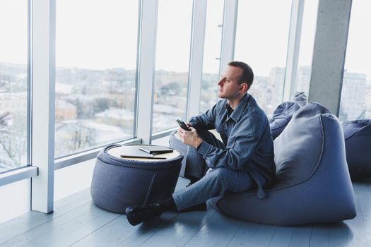 Confident male manager sitting in a modern workspace at a laptop and talking on the phone, remote work