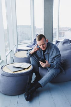A handsome European young businessman in a coffee shop sits with a mobile phone and makes notes in a notebook. Wearing an elegant casual suit and sitting with a laptop in a public cafe