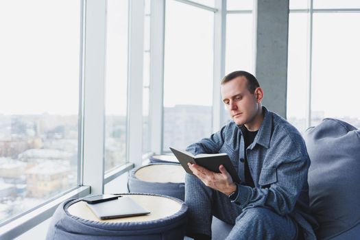 A male businessman in a casual suit resting in a comfortable pouf while working, an attractive freelancer in a suit works remotely and checks notes in a notebook