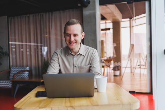 A young man sits at a table and opens a laptop computer while studying online. Modern digital computer works as a freelancer on a netbook in a cafe interior