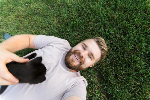 Man with little kitten lying and playing on grass - friendship love animals and pet owner