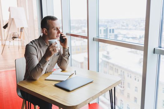 A young smart man is sitting in the office with a cup of coffee and is working on a project related to public cyber technology. Businessmen with laptop trying to meet deadlines in external marketing.