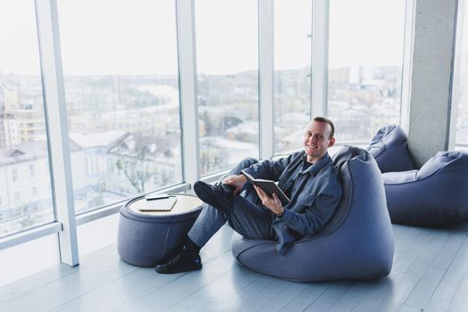 A male businessman in a casual suit resting in a comfortable pouf while working, an attractive freelancer in a suit works remotely and checks notes in a notebook
