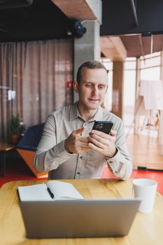 A young smart man is sitting in the office with a cup of coffee and is working on a project related to public cyber technology. Businessmen with laptop trying to meet deadlines in external marketing.