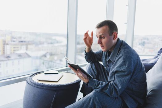A male businessman in a casual suit resting in a comfortable pouf while working, an attractive freelancer in a suit works remotely and checks notes in a notebook