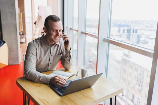 Intelligent young male using laptop to take notes during online education program, experienced male freelancer sitting with technology in cafe interior. Young businessman
