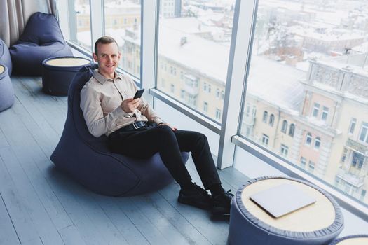 Successful male freelancer sitting in modern workspace and checking notifications on mobile phone in casual clothes. Remote work.