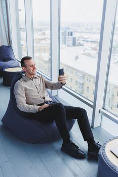 Successful male freelancer sitting in modern workspace and checking notifications on mobile phone in casual clothes. Remote work.