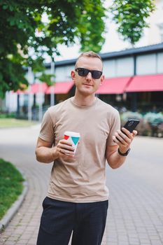A bearded, smiling, stylish man in white shirt and sunglasses standing on the streets of the city and calling on mobile phone.