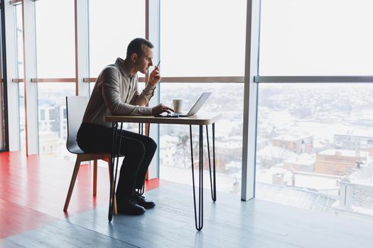 Smart young man looking for information on a website and working as a freelancer on developing a graphic project on a modern laptop using a wireless internet connection in a cafe interior