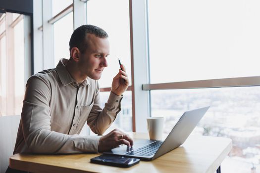 Smart young man looking for information on a website and working as a freelancer on developing a graphic project on a modern laptop using a wireless internet connection in a cafe interior