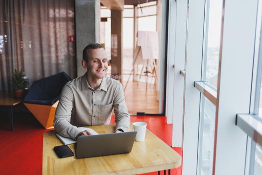 Smart young man looking for information on a website and working as a freelancer on developing a graphic project on a modern laptop using a wireless internet connection in a cafe interior