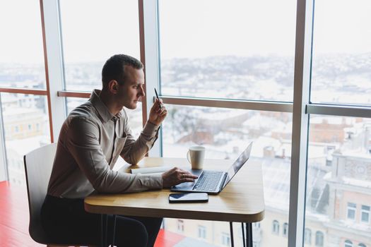 Smart young man looking for information on a website and working as a freelancer on developing a graphic project on a modern laptop using a wireless internet connection in a cafe interior