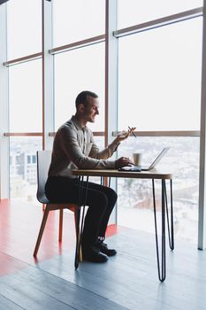 A young man sits at a table and opens a laptop computer while studying online. Modern digital computer works as a freelancer on a netbook in a cafe interior