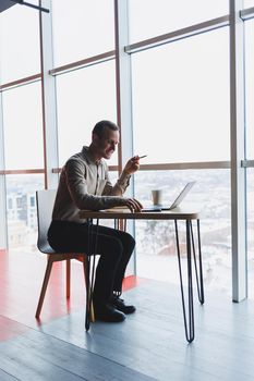 Smart young man looking for information on a website and working as a freelancer on developing a graphic project on a modern laptop using a wireless internet connection in a cafe interior