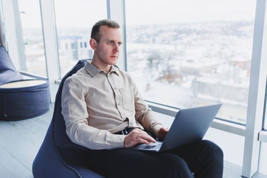 Concentrated young businessman looking at laptop screen, information online or working remotely online at home office, communicating remotely with client or study.