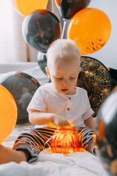 Children's Halloween - a boy in a carnival costume with orange and black balloons at home. Ready to celebrate Halloween.