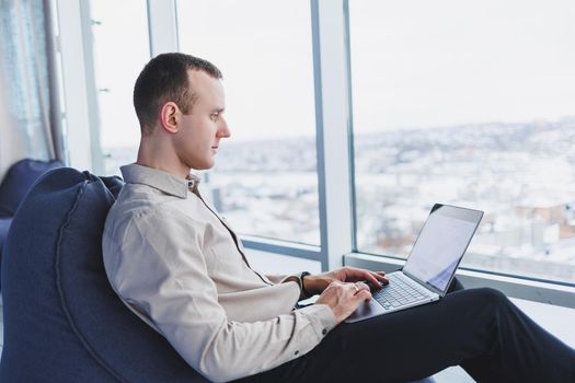 Concentrated young businessman looking at laptop screen, information online or working remotely online at home office, communicating remotely with client or study.