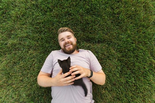 Man with little kitten lying and playing on grass - friendship love animals and pet owner