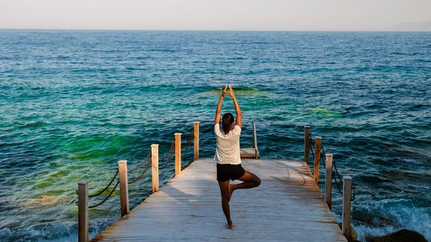 women practicing yoga on a wooden pier by the ocean during sunset in Turkey on vacation