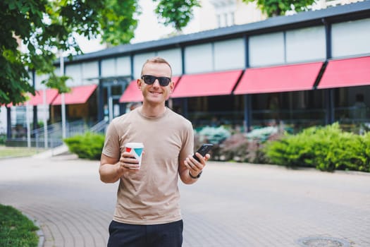 A bearded, smiling, stylish man in white shirt and sunglasses standing on the streets of the city and calling on mobile phone.
