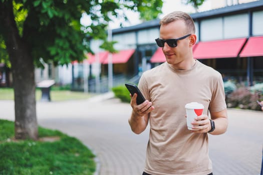 A bearded, smiling, stylish man in white shirt and sunglasses standing on the streets of the city and calling on mobile phone.