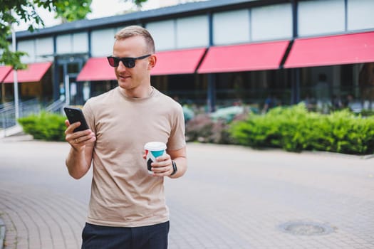 A bearded, smiling, stylish man in white shirt and sunglasses standing on the streets of the city and calling on mobile phone.