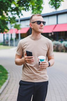 A bearded, smiling, stylish man in white shirt and sunglasses standing on the streets of the city and calling on mobile phone.