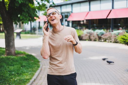 Portrait of handsome mature businessman holding messenger bag, wearing stylish eyeglasses looking at camera. Smiling middle aged man using smartphone, standing on the street. Mobile banking concept