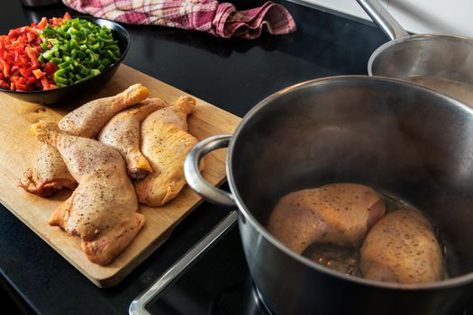 chicken being fried in a pot, to cook it with the vegetables that are chopped on the plate on the wooden board, and the soup in the other pot