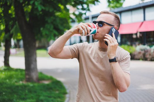 A bearded, smiling, stylish man in white shirt and sunglasses standing on the streets of the city and calling on mobile phone.