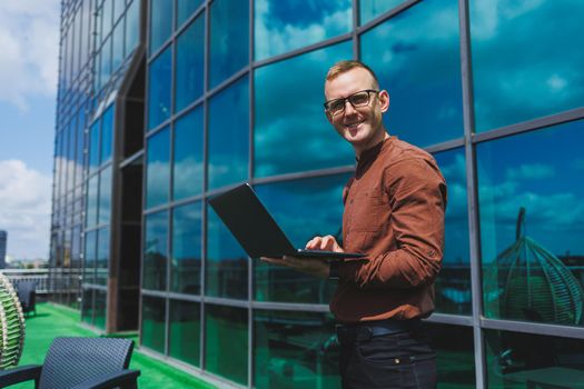 Cheerful businessman, formally dressed, pleased with received good news about contract details, sitting on office terrace with laptop, successful male entrepreneur