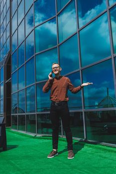 Happy man in classic glasses for vision correction with talking on terrace on mobile phone, smiling blogger browsing social media website