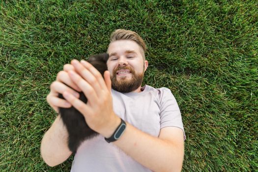 Man with little kitten lying and playing on grass - friendship love animals and pet owner