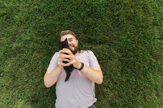 Man with little kitten lying and playing on grass - friendship love animals and pet owner