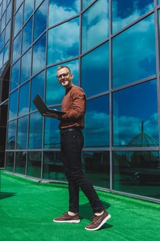 Cheerful businessman, formally dressed, pleased with received good news about contract details, sitting on office terrace with laptop, successful male entrepreneur