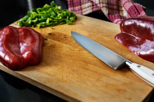 old wooden cutting board with a chef's knife, chopped green pepper, a red pepper cut in half and a napkin