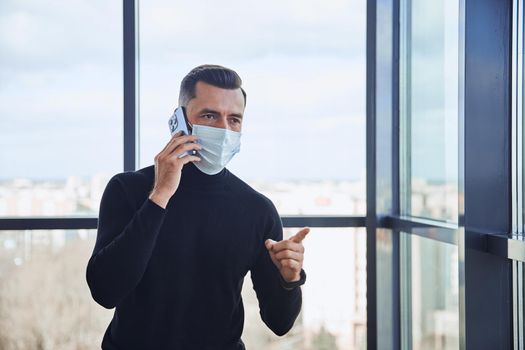 businessman with a smartphone standing near a large office window.