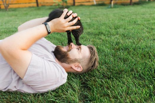 Man with little kitten lying and playing on grass - friendship love animals and pet owner