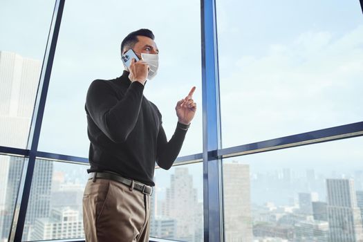 businessman with a smartphone standing near a large office window.