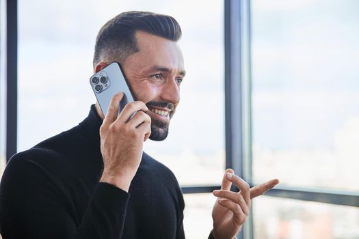 businessman with a smartphone standing near a large office window.