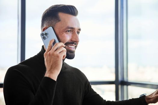 man in a protective mask talking on a smartphone standing near the window.