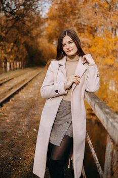 A beautiful long-haired woman walks through the autumn streets. Railway, autumn leaves, a woman in a light coat.