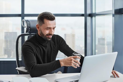 tired businessman drinks coffee sitting at his desk. close-up.