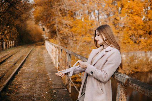 A beautiful long-haired woman walks through the autumn streets. Railway, autumn leaves, a woman in a light coat.