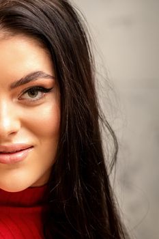 The fashionable young woman. Portrait of the beautiful female model with long hair and makeup. Beauty young caucasian woman with a brown curly hairstyle on the background of a gray wall